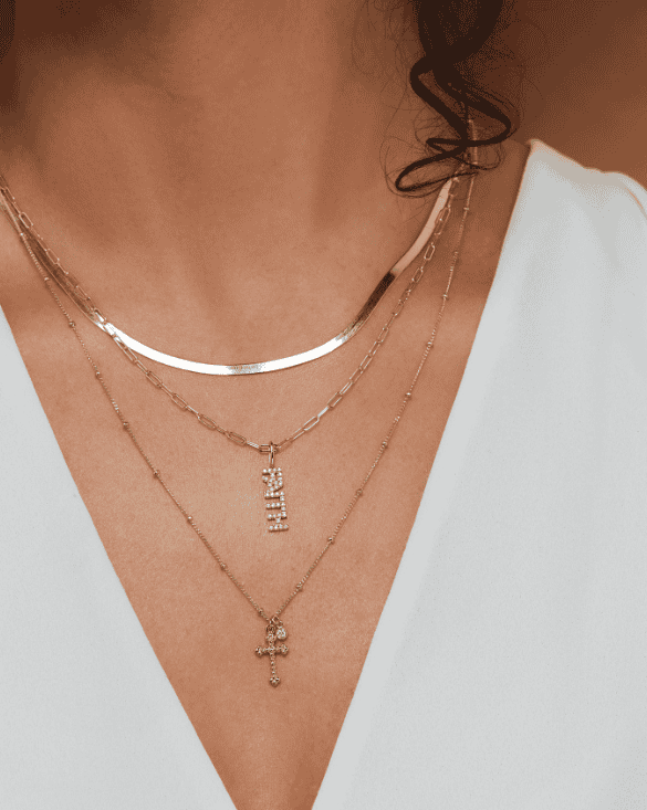 A woman smiles, highlighting Winter Jewelry’s elegant gold necklaces that add a stylish touch to her simple outfit.