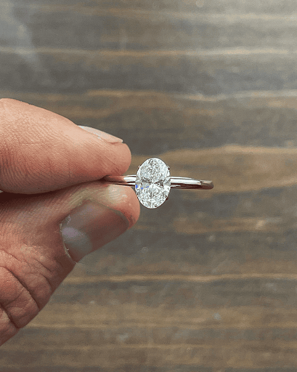 A hand shows a simple oval diamond ring from Winter Jewelry, highlighting its beauty and quality.